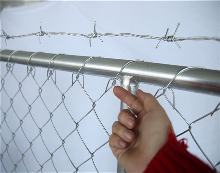 Ręka wskazuje drut baebed na szczycie ogrodzenia z ogniw łańcucha