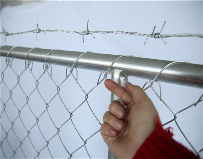 A hand points up the baebed wire at top of chain link fence