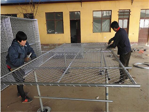 Two workers twine the wire to the chain link mesh on the Frame Tube