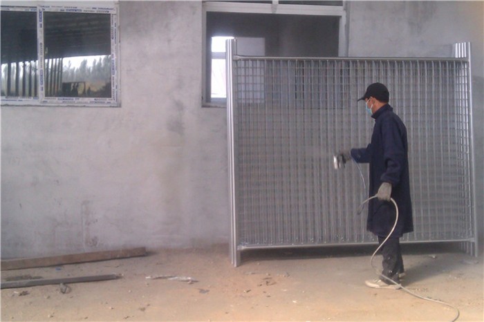 a worker is painting the silver color on the temporary fence panels