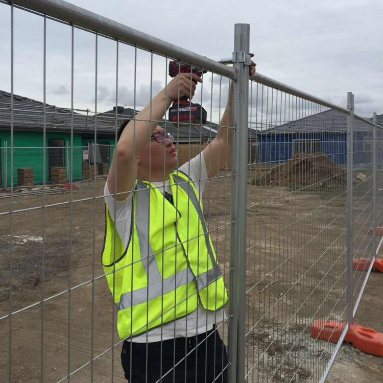 a worker is installing the steel clamps onto thetemporary fence panels