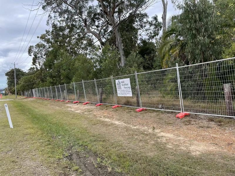 Les panneaux de clôture temporaires australiens installés avec des pieds en plastique orange sur un chantier de construction.