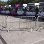 Galvanized steel crowd control barriers with interlocking systems securing a bus station, filled with spectators.