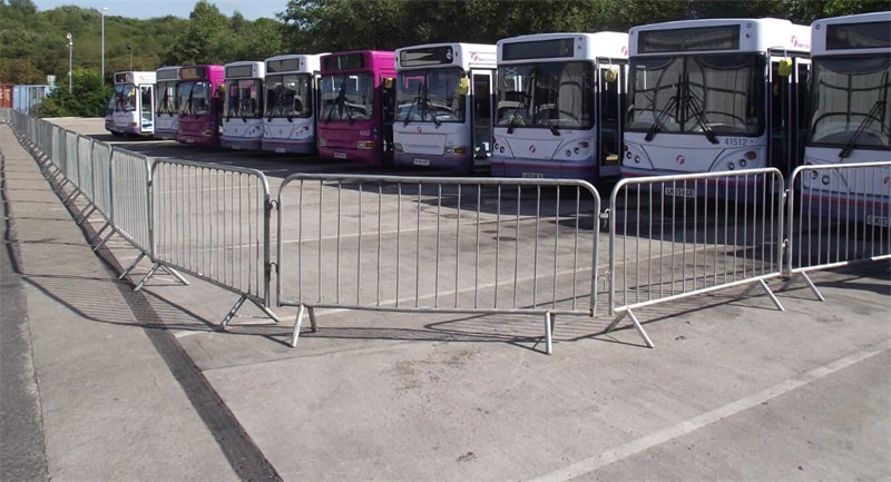 Galvanized steel crowd control barriers with interlocking systems securing a bus station, filled with spectators.