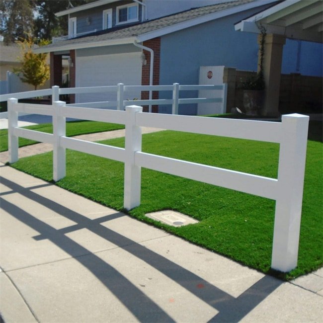 A white PVC fence with two horizontal rails, installed around a neatly maintained lawn in a residential neighborhood. The fence provides a clean, modern look and enhances the property's curb appeal.