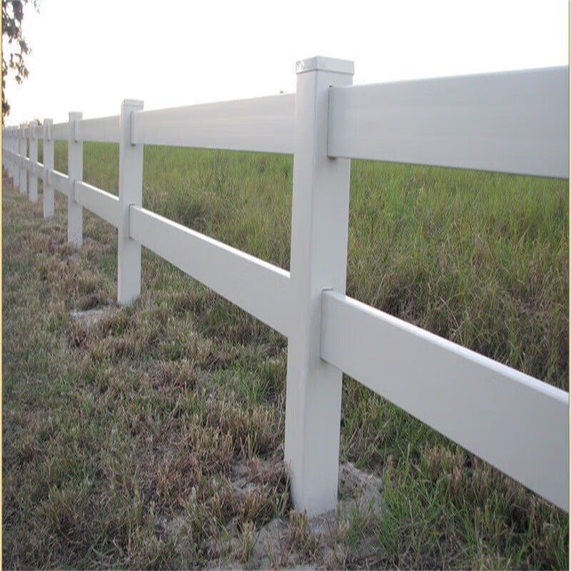 A white PVC arena fencing with two horizontal rails, installed along the perimeter of a grassy field. The fencing provides a sturdy and visually appealing boundary suitable for horse arenas or other enclosures.
