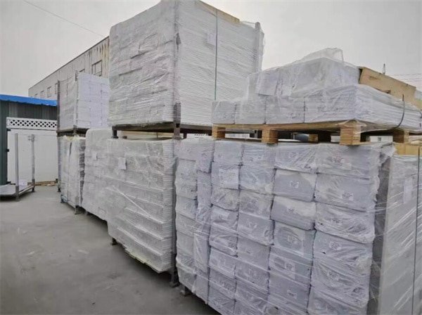 Stacks of packaged PVC horse arena fencing materials wrapped in plastic, ready for shipment. The bundles are organized on wooden pallets and stored in an outdoor area, showcasing the neatly packed and prepared fencing components.