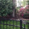 Black aluminum fence installed around a lush garden with blooming flowers and tall trees, enhancing both security and aesthetics.