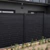 Elegant black aluminium slat fence installed in a garden, featuring horizontal slats and vertical posts on a stone base.