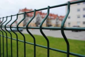 Close-up of a green welded wire fence with a residential area in the background, demonstrating the fence's application in urban environments for property boundaries and security.