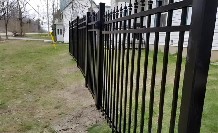 Um longo trecho de cerca de alumínio preta com ponta de lança instalada ao longo do perímetro de uma propriedade residencial.