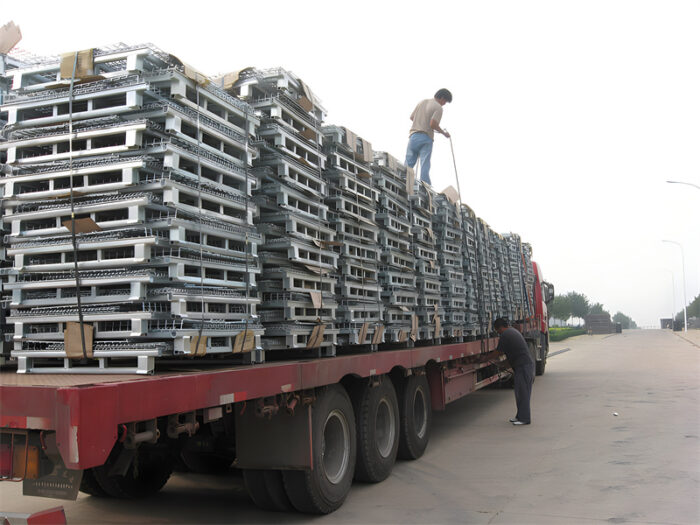 Camion chargé de cages de stockage empilées et pliables, sécurisées pour le transport par les travailleurs.