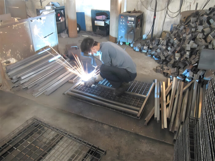 Worker welding parts of a stillage cage, showcasing the manufacturing process.