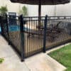 Black aluminum flat top fence with decorative rings installed around a garden pool area, surrounded by lush greenery and palm trees.