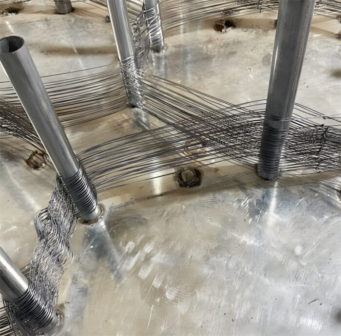 Workers assembling tank track mesh in a production facility, showcasing the precise arrangement of durable metal wires on specialized equipment, essential for creating robust anti-tank barriers.