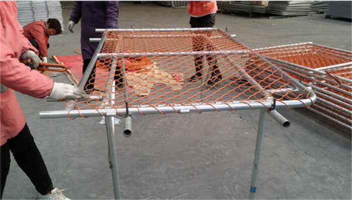 Les ouvriers attachent le fil au tube du cadre de la clôture de la barrière de chantier.