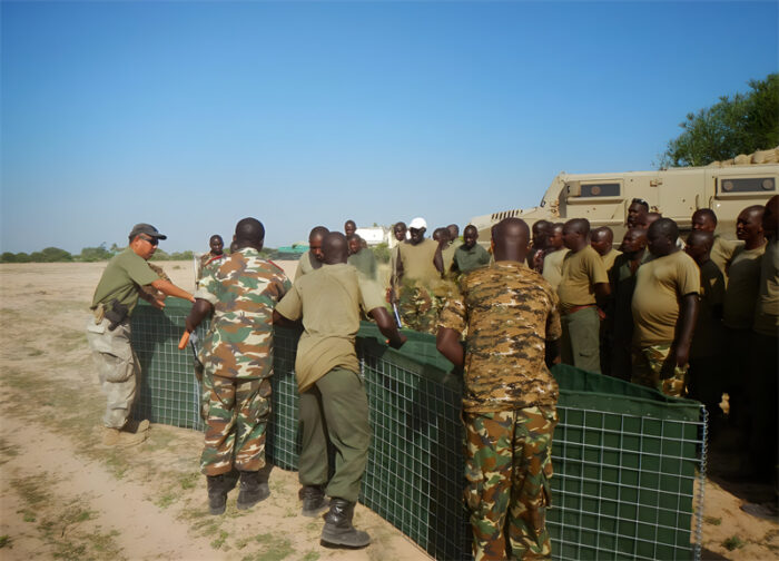 Des soldats assemblent une barrière verte Hesco sur un terrain d'entraînement.