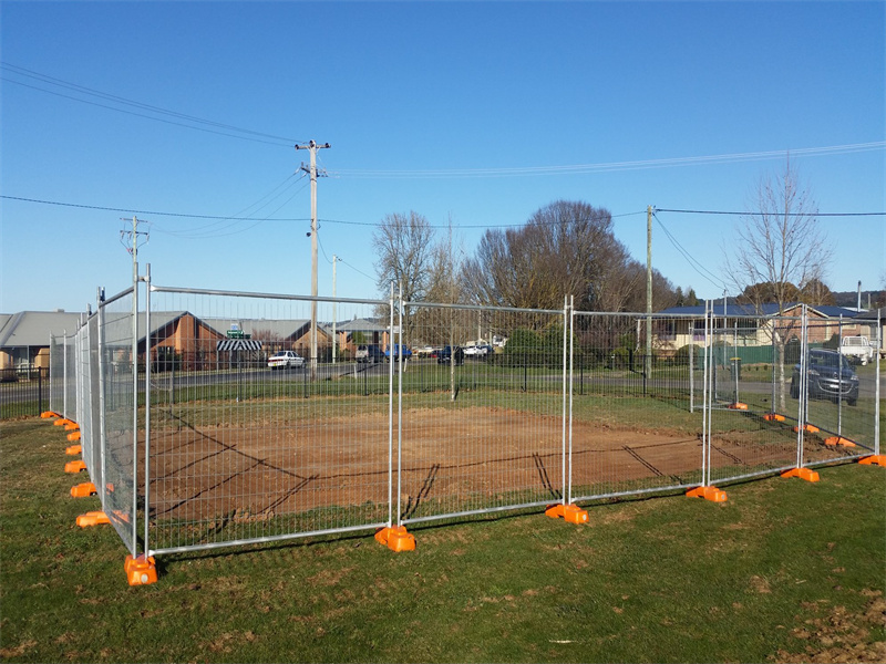 Temporary Fence Installation on a Field: A temporary fence structure set up on a grassy field with orange bases, providing a secure perimeter around an empty area.