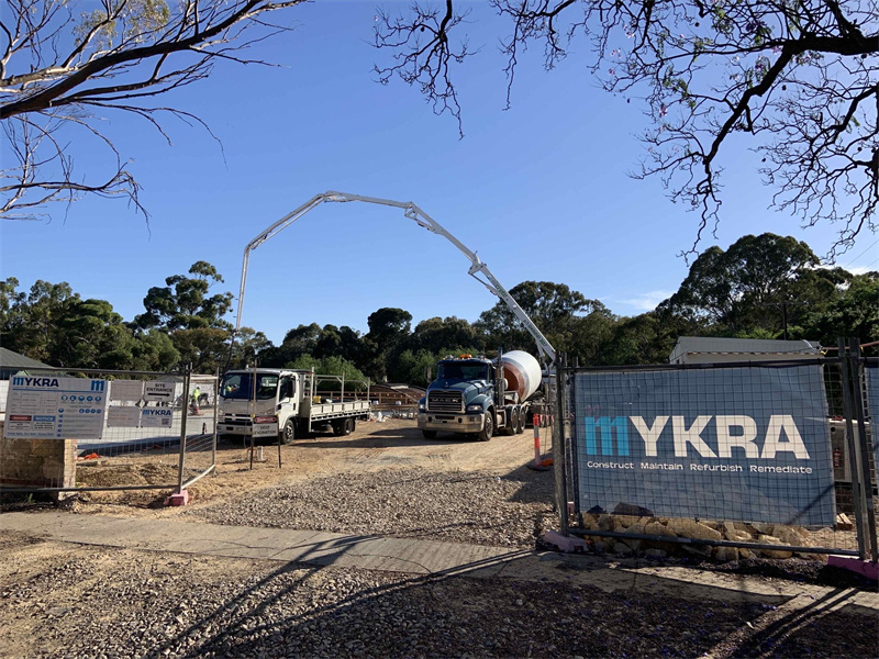 A construction site entrance with temporary fencing and a concrete mixer truck in view.