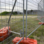 Close-up of a temporary fencing setup with orange plastic feet for stability on a construction site.