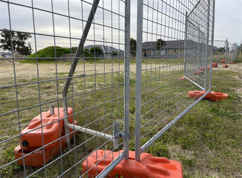 Close-up of a temporary fencing setup with orange plastic feet for stability on a construction site.