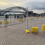 Temporary Fence Setup near an Urban Landmark: Temporary fencing with yellow bases set up in a public plaza with a famous bridge in the background.