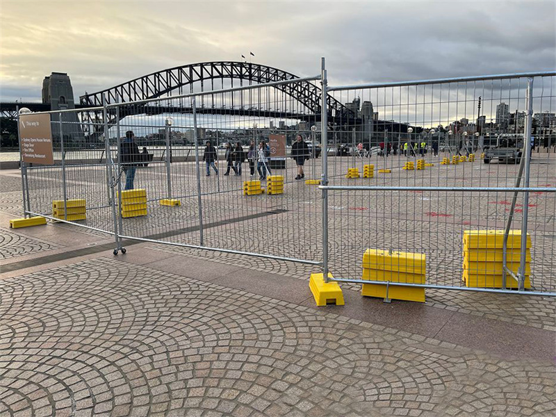 Temporary Fence Setup near an Urban Landmark: Temporary fencing with yellow bases set up in a public plaza with a famous bridge in the background.