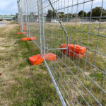 Close-up view of temporary fencing secured by bright orange bases, illustrating effective stability measures.