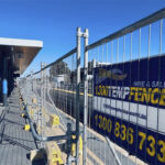 Temporary fencing at a public location with a banner displaying contact information for 1300 Temp Fence.