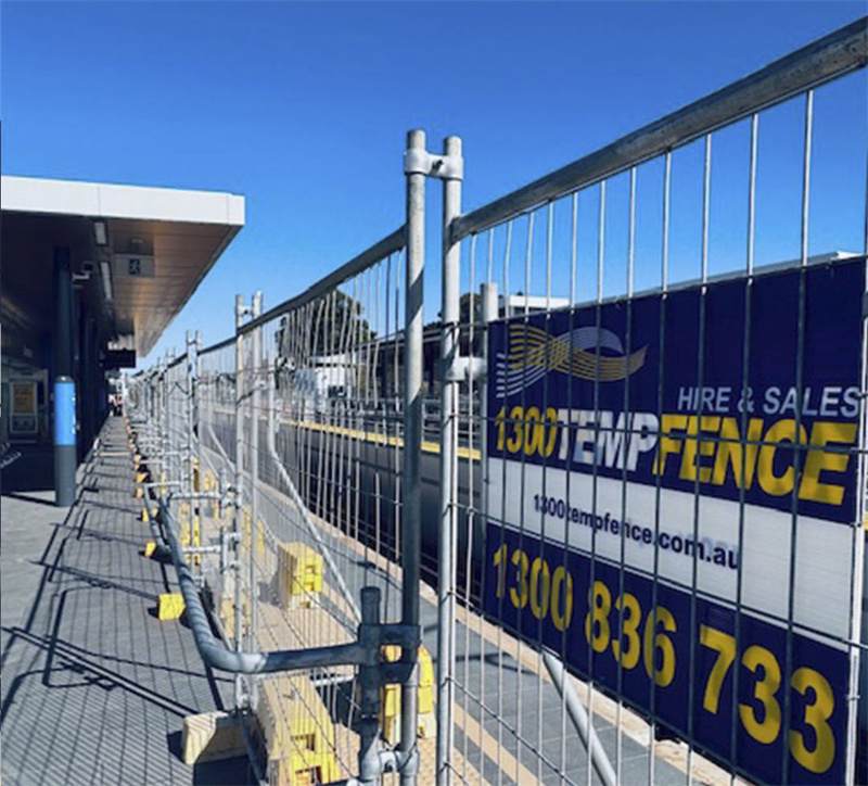 Temporary fencing at a public location with a banner displaying contact information for 1300 Temp Fence.