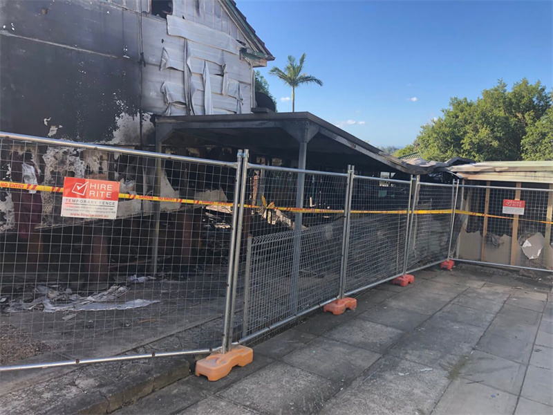 Temporary fencing enclosing a fire-damaged building site under repair with visible warning signage.