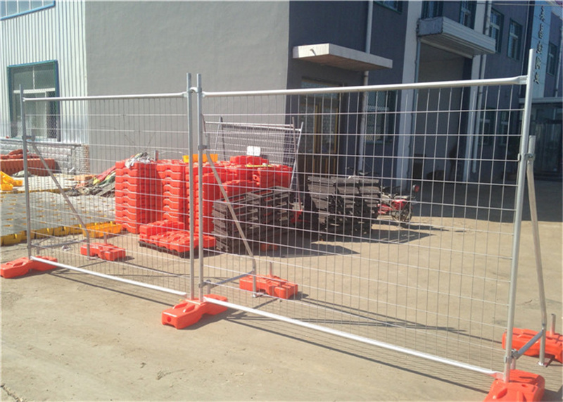 A temporary fencing setup at a construction site, showing the panels supported by orange bases and adjacent to stored equipment.