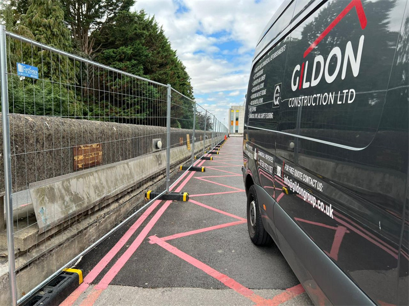 Construction site with temporary fencing set up beside a van, featuring marked pathways for efficient access.