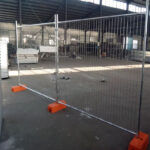 Temporary fencing setup inside a facility, showing strong support with orange bases for secure installation.