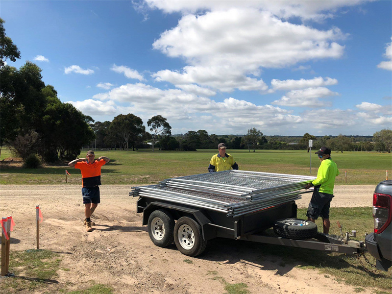 Three workers unloading temporary fencing panels from a trailer at an event site in Australia.