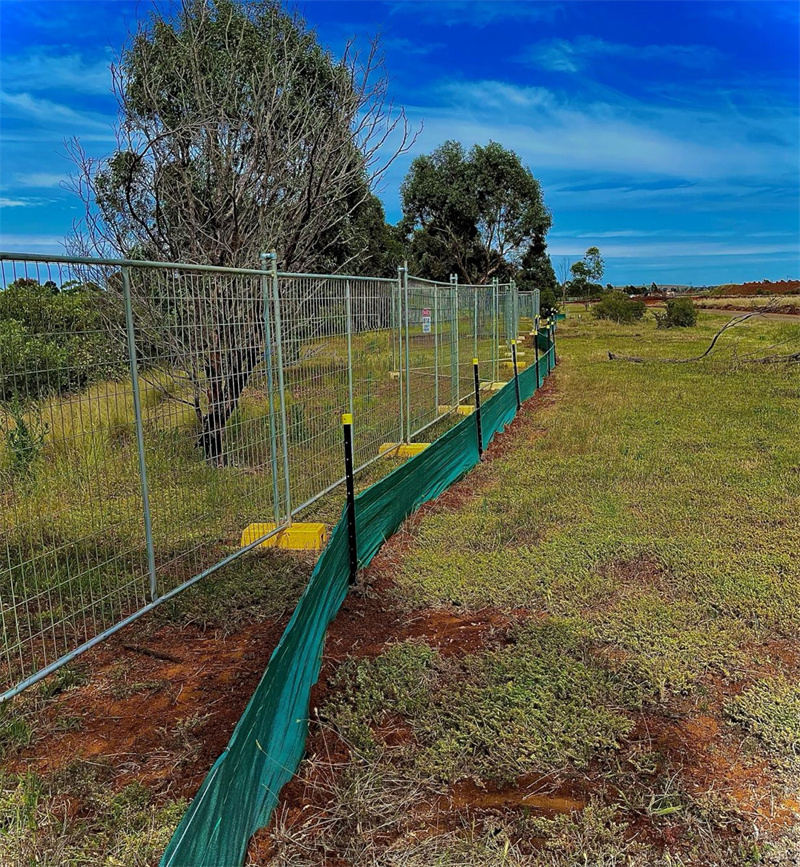 Temporary fencing enclosing a large outdoor area with a visible tree line in the background.