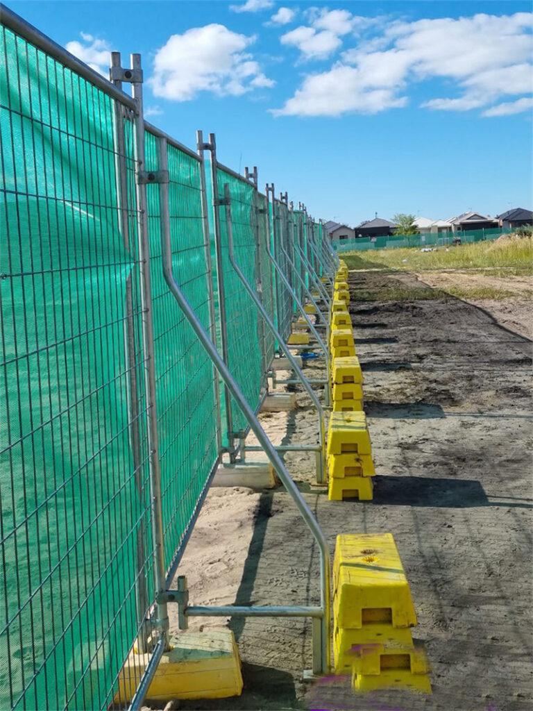 Green mesh-covered fence supported by yellow bases at a construction site.