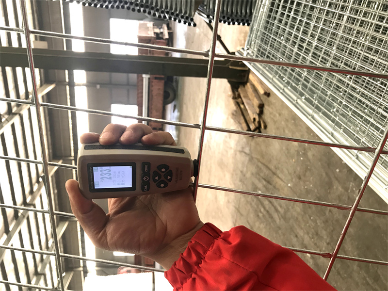 A person holds a digital measurement device next to a wire fence in a warehouse. The device displays a value of 263.