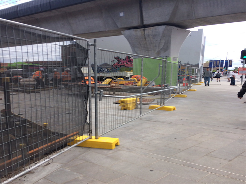 Industrial Temporary Fencing on a Construction Site: Temporary fencing with yellow bases, set up along a construction area beside an overpass.