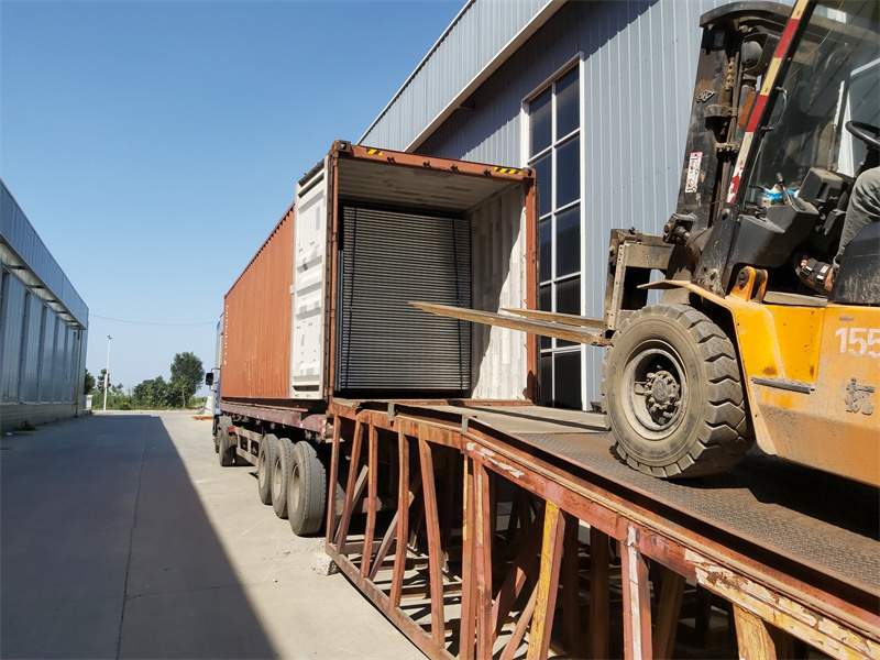 Forklift unloading metal panels from a shipping container on a flatbed truck.