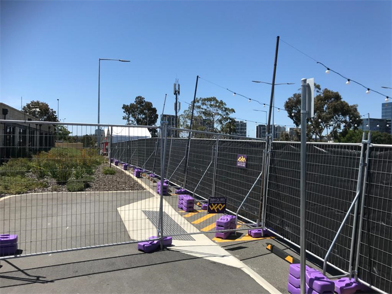 Event area with black mesh fencing and purple bases, set along a sidewalk path.