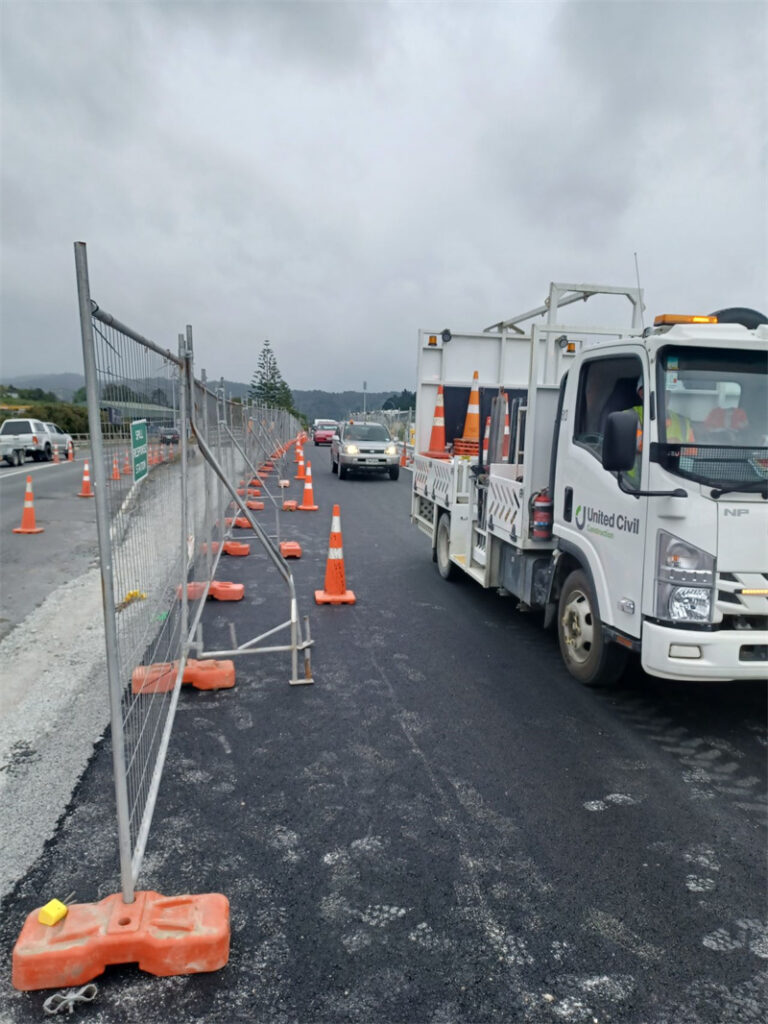 Roadside construction with temporary fencing and orange cones, alongside a United Civil truck.