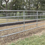 A shiny metal horse panel installed in an outdoor setting with gravel ground, designed for secure containment.