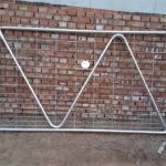 A galvanized gate with a diagonal brace set against a brick wall, showcasing its sturdy design and readiness for installation.