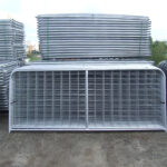 Multiple stacked metal gates grouped together in a storage area with a cloudy sky in the background.