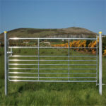 A close-up of a galvanized steel farm gate with a scenic hillside background, emphasizing its practical use and aesthetic appeal on a farm.