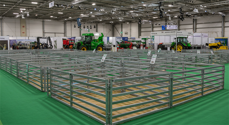 An exhibition area showcasing galvanized sheep panels set up with various machinery, demonstrating agricultural techniques at a trade show.