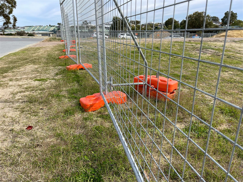 Close-up of temporary fencing with orange bases securely placed on grassy terrain, showing stability and durability.