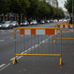 Steel barricades with orange and white stripes positioned on a busy road, directing traffic and ensuring pedestrian safety during an event.