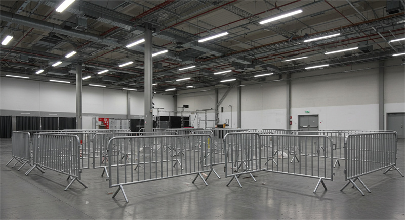 An indoor venue featuring steel crowd control barriers arranged in a circular layout, preparing for an event with ample space for attendees and equipment.